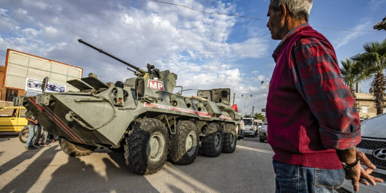Un hombre mira cómo un vehículo blindado de la policía militar rusa pasa por una calle en la ciudad de Amuda, en el noreste de Siria, en la provincia de Hasakeh, el 24 de octubre de 2019, como parte de una patrulla conjunta entre las fuerzas rusas y las fuerzas de seguridad internas de los kurdos sirios cerca de la frontera con Pavo. (Delil SOULEIMAN / AFP)