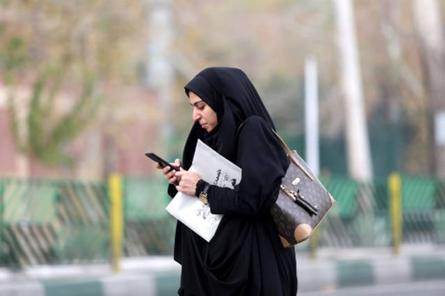 Una mujer usa un teléfono inteligente mientras está de pie en una calle de la capital iraní, Teherán, el 23 de noviembre de 2019. - Los iraníes han estado luchando por adaptarse a la vida fuera de línea casi una semana en un apagón de Internet casi total impuesto en medio de manifestaciones violentas que han obligado a algunos a recurrir a las viejas formas de sobrevivir. (Foto por ATTA KENARE / AFP)