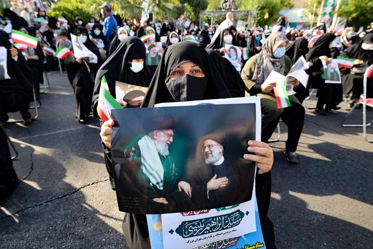 Un partidario del candidato presidencial ultraconservador iraní Ebrahim Raisi lleva un cartel con una foto suya con el líder supremo de Irán, el ayatolá Alí Jamenei, durante un mitin en la capital, Teherán, el 16 de junio de 2021 (ATTA KENARE / AFP)