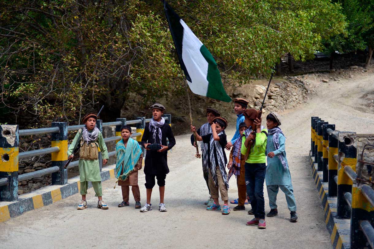 Niños de residentes afganos locales portando rifles de caza y una bandera sobre un puente en el área de Bandejoy del distrito de Dara, en la provincia de Panjshir, el 21 de agosto de 2021, días después de la sorprendente toma de posesión de Afganistán por parte de los talibanes. (Ahmad SAHEL ARMAN / AFP)