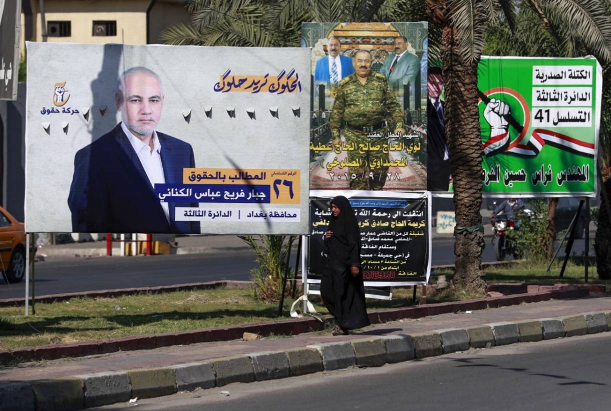 Una mujer iraquí camina delante de los carteles electorales de los candidatos a las próximas elecciones parlamentarias, en el barrio de Ciudad Sadr de la capital, Bagdad, el 9 de octubre de 2021. (AHMAD AL-RUBAYE / AFP)