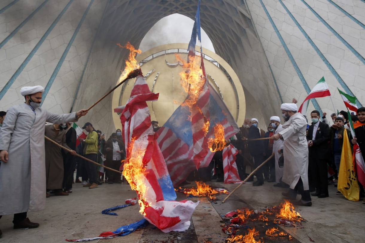 Los clérigos queman representaciones de la bandera de EE. UU. bajo la torre del monumento Azadi (libertad) durante la manifestación anual que conmemora el aniversario de la Revolución Islámica de Irán de 1979, en Teherán, Irán, el viernes 11 de febrero de 2022 (AP Photo/Vahid Salemi)