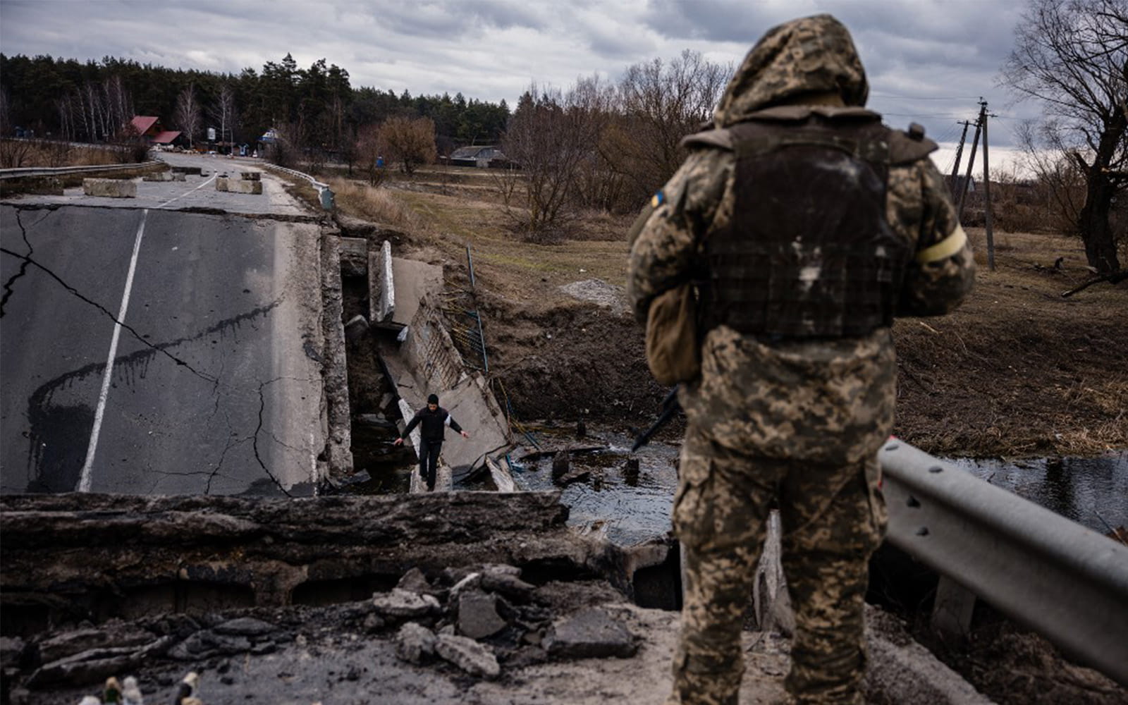 Un soldado ucraniano mira a un civil que cruza un puente volado en un pueblo al este de la ciudad de Brovary, Ucrania, el 6 de marzo de 2022. (Dimitar Dilkoff/AFP)