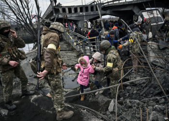 La gente cruza un puente destruido mientras evacua la ciudad de Irpin, al noroeste de Kiev, durante un intenso bombardeo el 5 de marzo de 2022, 10 días después de que Rusia lanzara una invasión militar en Ucrania. (Aris Messinis/AFP)