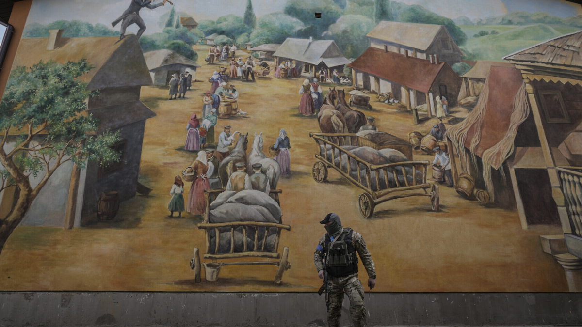 Un miembro del equipo de seguridad camina junto a un mural temático de Fidler on the Roof en el asentamiento judío de Anatevka, a las afueras de Kiev, Ucrania, el 27 de marzo de 2022. (AP Photo/Vadim Ghirda)