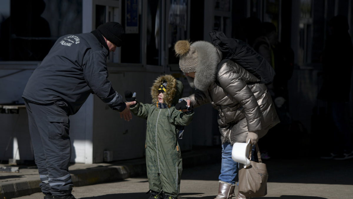 Un empleado de aduanas tiende la mano a un niño refugiado que huye de la guerra de la vecina Ucrania con su familia en el paso fronterizo, en la frontera rumano-ucraniana, en Siret, Rumanía, el 11 de marzo de 2022. (AP Photo/Andreea Alexandru)