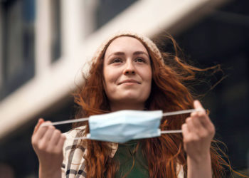 Retrato de una joven feliz quitándose la mascarilla al aire libre en la ciudad, la vida después del covid-19.