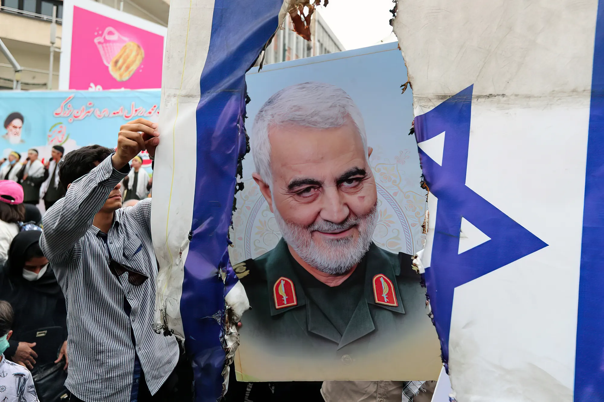 Los iraníes se preparan para prender fuego a una bandera israelí junto a una foto del difunto general iraní Qasem Soleimani durante una manifestación para celebrar el día de al-Quds (Jerusalén) en Teherán, el 29 de abril de 2022 (AFP)