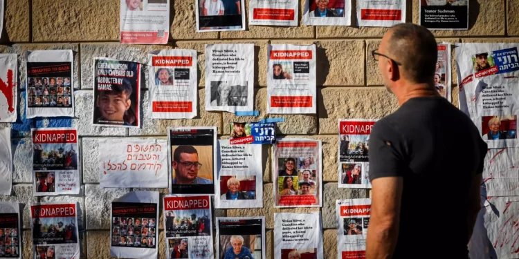 Varias personas caminan cerca de carteles en los que aparecen israelíes retenidos como rehenes por Hamás en Gaza, frente al Ministerio de Defensa en Tel Aviv, 18 de octubre de 2023. (Chaim Goldberg/Flash90)