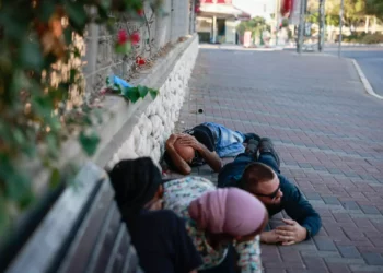 La gente se pone a cubierto en la carretera en el sur de la ciudad israelí de Ashkelon, mientras suena una alerta de sirena roja, 10 de octubre de 2023.(Chaim Goldberg/Flash90)