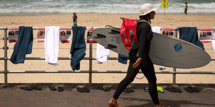 Una surfista con su tabla pasa junto a carteles, toallas y chanclas que forman parte de una protesta organizada por la comunidad judía australiana en la playa de Bondi, en Sídney, el 2 de noviembre de 2023, para poner de relieve la difícil situación de los rehenes retenidos por Hamás (Foto de DAVID GRAY / AFP)