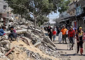 Hombres heridos caminan con muletas junto a niños sentados sobre los escombros de un edificio derrumbado en una calle de Rafah, en el sur de la Franja de Gaza, el 9 de abril de 2024. (AFP)