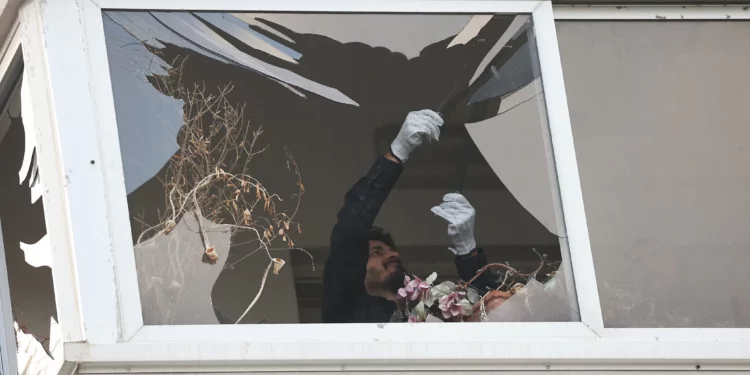 Un policía recoge metralla de vidrio de la ventana de un edificio dañado por un ataque con drones en Tel Aviv el 19 de julio de 2024 (GIL COHEN-MAGEN / AFP)