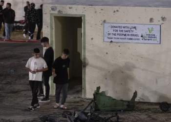 Jóvenes caminan junto a un refugio dañado por la metralla en un campo de fútbol que fue alcanzado por un cohete, matando a varios niños y adolescentes, en la ciudad drusa de Majdal Shams, en los Altos del Golán, el 27 de julio de 2024. (Foto AP/Leo Correa)