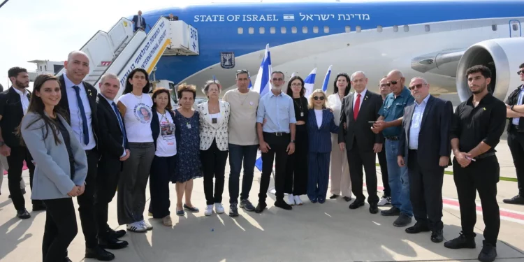 El primer ministro, Benjamin Netanyahu, y su séquito, así como las familias de los rehenes retenidos por Hamás en Gaza (Noa Argamani y su padre Yaakov están en el centro, junto a Sara Netanyahu) posan frente al avión oficial de Wing of Zion antes de partir hacia Washington, DC, en el aeropuerto Ben Gurion, el 22 de julio de 2024. (Amos Ben Gershom/GPO)