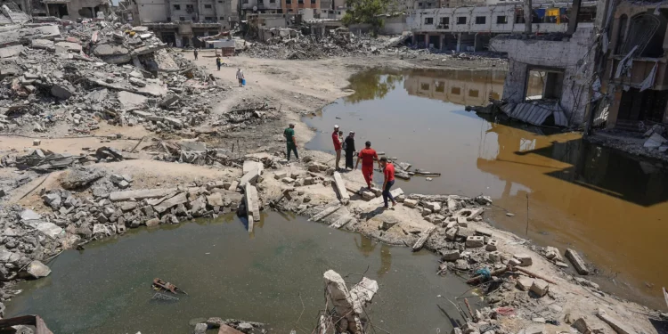 Palestinos caminan sobre los escombros de edificios destruidos, entre dos charcos de agua estancada en Jan Yunis, en el sur de la Franja de Gaza, el 19 de julio de 2024 (Bashar TALEB / AFP)