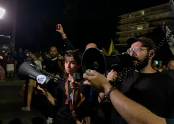 El activista antigubernamental Tomer Lev da un discurso improvisado en el que ordena a los manifestantes marchar en silencio hacia la residencia del primer ministro Benjamin Netanyahu, en vista del mortal ataque de Hezbolá en los Altos del Golán, el 27 de julio de 2024. (Charlie Summers/Times of Israel)