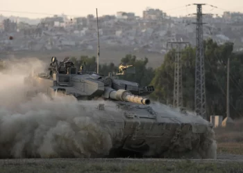Con edificios destruidos en la Franja de Gaza a sus espaldas, un soldado israelí saluda desde un tanque, cerca de la frontera entre Israel y Gaza, en el sur de Israel, el 1 de agosto de 2024. (Foto AP/Tsafrir Abayov)