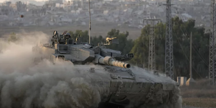 Con edificios destruidos en la Franja de Gaza a sus espaldas, un soldado israelí saluda desde un tanque, cerca de la frontera entre Israel y Gaza, en el sur de Israel, el 1 de agosto de 2024. (Foto AP/Tsafrir Abayov)