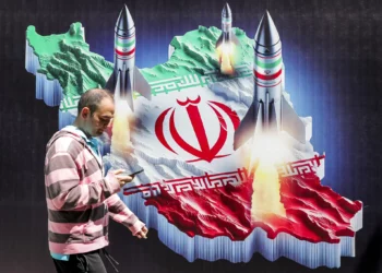 Un hombre pasa junto a una pancarta que muestra el lanzamiento de misiles desde una representación del mapa de Irán coloreado con la bandera iraní en el centro de Teherán, el 15 de abril de 2024. (ATTA KENARE / AFP)
