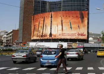 Un hombre cruza una calle mientras los automovilistas pasan frente a una valla publicitaria que muestra misiles balísticos iraníes en servicio en Teherán el 19 de abril de 2024. (AFP)