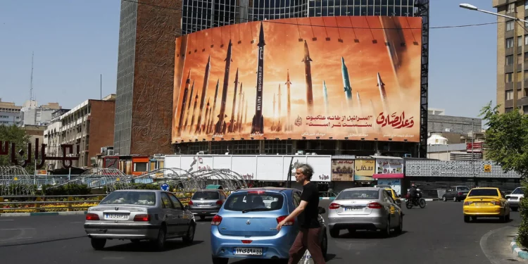 Un hombre cruza una calle mientras los automovilistas pasan frente a una valla publicitaria que muestra misiles balísticos iraníes en servicio en Teherán el 19 de abril de 2024. (AFP)