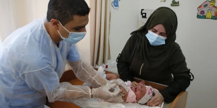 Un empleado de la UNRWA, que lleva una mascarilla debido a la pandemia del coronavirus COVID-19, administra la vacuna contra la polio y el rotavirus a niños en una clínica del campo de refugiados de Bureij, en el centro de la Franja de Gaza, el 9 de septiembre de 2020. (Mohammed ABED / AFP)