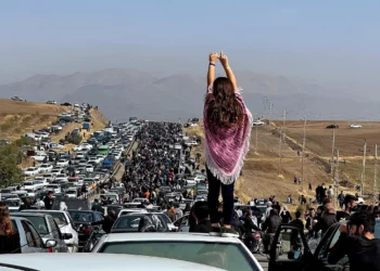 This UGC image posted on Twitter reportedly on October 26, 2022 shows an unveiled woman standing on top of a vehicle as thousands make their way towards Aichi cemetery in Saqez, Mahsa Amini's home town in the western Iranian province of Kurdistan, to mark 40 days since her death. (Photo by UGC / AFP)