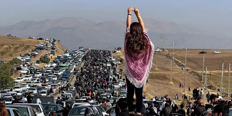 This UGC image posted on Twitter reportedly on October 26, 2022 shows an unveiled woman standing on top of a vehicle as thousands make their way towards Aichi cemetery in Saqez, Mahsa Amini's home town in the western Iranian province of Kurdistan, to mark 40 days since her death. (Photo by UGC / AFP)