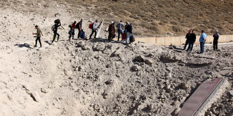 Personas que huyen de los intensos combates en Líbano caminan alrededor de un cráter causado por un ataque israelí contra la infraestructura de contrabando de armas de Hezbolá, en el área del cruce fronterizo de Masnaa, en Líbano, con Siria, el 4 de octubre de 2024. (Hassan Jarrah / AFP)