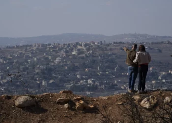 Una pareja israelí observa los edificios dañados en una aldea en el sur del Líbano, cerca de la frontera entre Israel y el Líbano, durante el alto el fuego entre Israel y Hezbolá, en el norte de Israel, el sábado 30 de noviembre de 2024. (Foto AP/Leo Correa)