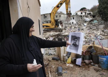 Una mujer sostiene un retrato de su nieto, un combatiente de Hezbolá que murió en los combates con las tropas israelíes, mientras espera que los rescatistas recuperen su cuerpo de debajo de los escombros de una casa destruida, al fondo, en la aldea de Ainata, en el sur del Líbano, tras un alto el fuego entre Israel y Hezbolá el 27 de noviembre de 2024. (Foto AP/Hussein Malla)