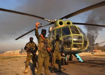 Combatientes anti-régimen posan para una fotografía con un helicóptero del ejército en la pista del aeropuerto militar de Nayrab, en la ciudad de Alepo, en el norte de Siria, el 2 de diciembre de 2024. (Aaref Watad/AFP)