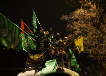 Hombres palestinos ondeando banderas de Hamás (verde) y Hezbolá (amarilla) sentados en la parte superior de un autobús de la Cruz Roja que transporta a terroristas presos liberados de la prisión militar de Ofer en Judea y Samaria son recibidos por una multitud de familiares y amigos en Beitunia, en las afueras de Ramallah, en las primeras horas del 20 de enero de 2025. (Foto de John Wessels / AFP)