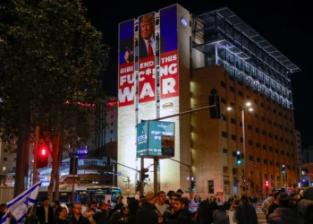 Un cartel que pide el fin de la guerra entre Israel y Hamás junto con un retrato del presidente electo de Estados Unidos, Donald Trump, se encuentra en la parte superior de un edificio cerca de una protesta de israelíes de derecha que rechazan un posible acuerdo con Hamás, en Jerusalén, el 13 de enero de 2025. (Foto de Menahem Kahana / AFP)