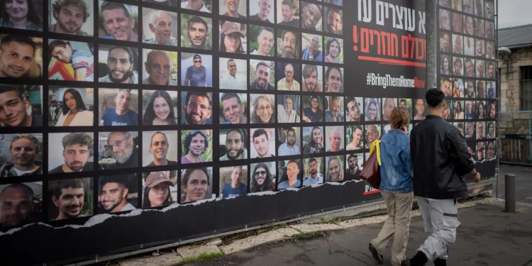 Personas caminando junto a fotografías de rehenes retenidos por terroristas de Hamás en Gaza, en Jerusalén, el 12 de enero de 2025 (Chaim Goldberg/Flash90