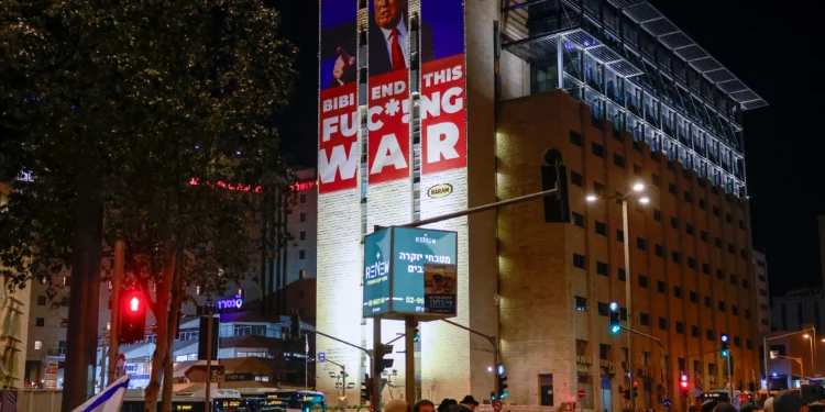 Un cartel que pide el fin de la guerra entre Israel y Hamás junto con un retrato del presidente electo de Estados Unidos, Donald Trump, se encuentra en la parte superior de un edificio cerca de una protesta de israelíes de derecha que rechazan un posible acuerdo con Hamás, en Jerusalén, el 13 de enero de 2025. (Foto de Menahem Kahana / AFP)