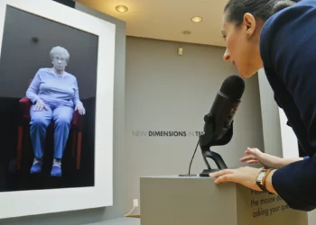 Ilustrativo: Josephine Mairzadeh utiliza un micrófono para plantear una pregunta a una presentación virtual de la sobreviviente del Holocausto Eva Schloss, que aparece en una instalación interactiva testimonial llamada “Nuevas dimensiones en el testimonio” en el Museo del Patrimonio Judío, en Nueva York, el 15 de septiembre de 2017. (Foto AP/Bebeto Matthews)