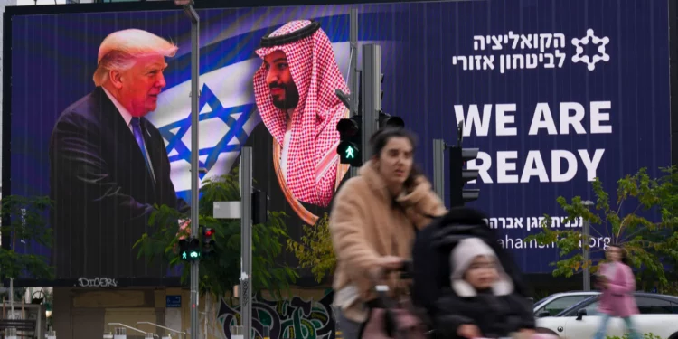 La gente pasa frente a un cartel electrónico que muestra al presidente de Estados Unidos, Donald Trump, a la izquierda, estrechando la mano del príncipe heredero saudí, Mohammed bin Salman, con un texto que dice: "Estamos listos", en Tel Aviv, el 3 de febrero de 2025. (Foto AP/ Ariel Schalit)