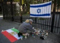 Una mujer enciende una vela para mostrar su apoyo frente a la embajada de Israel en Estocolmo, Suecia, el 9 de octubre de 2023, tras el ataque terrorista del 7 de octubre dirigido por Hamás contra Israel. En la valla hay una bandera israelí y en el suelo la histórica bandera de Irán. (Foto de Jonathan Nackstrand / AFP)