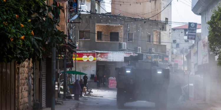 Palestinian shopkeepers look as Israeli armored vehicles drive by during a raid in the eastern neighborhood of Jenin amid a weeks-long operation in the West Bank on March 4, 2025. (Jaafar ASHTIYEH / AFP)