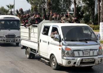 Security forces loyal to the interim Syrian government ride in the back of a vehicle moving along a road in Syria's western city of Latakia on March 9, 2025. (OMAR HAJ KADOUR / AFP)