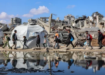 La gente pasa junto a un charco de agua junto a un refugio de tiendas de campaña erigido cerca de los escombros de un edificio derrumbado en el barrio de Nasr, en el oeste de la ciudad de Gaza, el 15 de abril de 2025. (Omar AL-QATTAA / AFP)