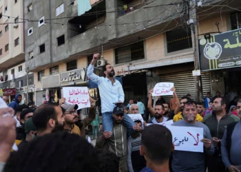 Gazatíes en Deir al-Balah, en el centro de la Franja de Gaza, sostienen carteles contra la guerra mientras un hombre canta consignas en apoyo a la población de Beit Lahiya, en el norte de Gaza, que ha estado protestando contra Hamás, el 26 de marzo de 2025. (AP/Abdel Kareem Hana)