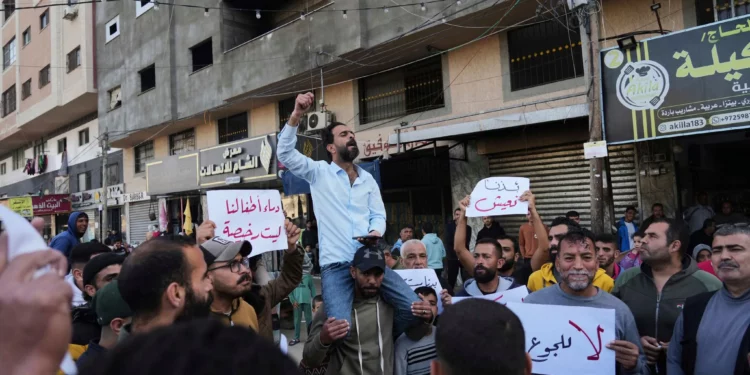 Gazatíes en Deir al-Balah, en el centro de la Franja de Gaza, sostienen carteles contra la guerra mientras un hombre canta consignas en apoyo a la población de Beit Lahiya, en el norte de Gaza, que ha estado protestando contra Hamás, el 26 de marzo de 2025. (AP/Abdel Kareem Hana)