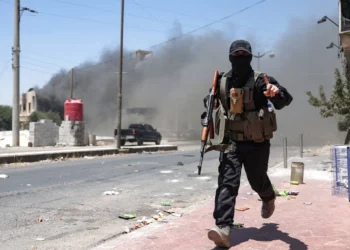 Una densa humareda se eleva mientras un miembro de las fuerzas beduinas y tribales corre durante los enfrentamientos con combatientes drusos en la ciudad de Sweida, en el sur de Siria, el 19 de julio de 2025. (OMAR HAJ KADOUR / AFP)