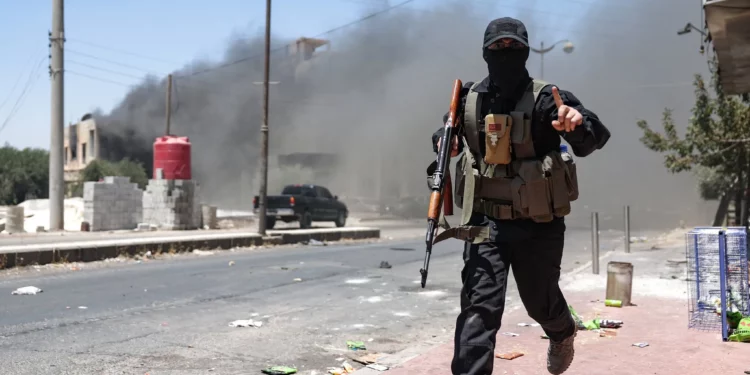Una densa humareda se eleva mientras un miembro de las fuerzas beduinas y tribales corre durante los enfrentamientos con combatientes drusos en la ciudad de Sweida, en el sur de Siria, el 19 de julio de 2025. (OMAR HAJ KADOUR / AFP)