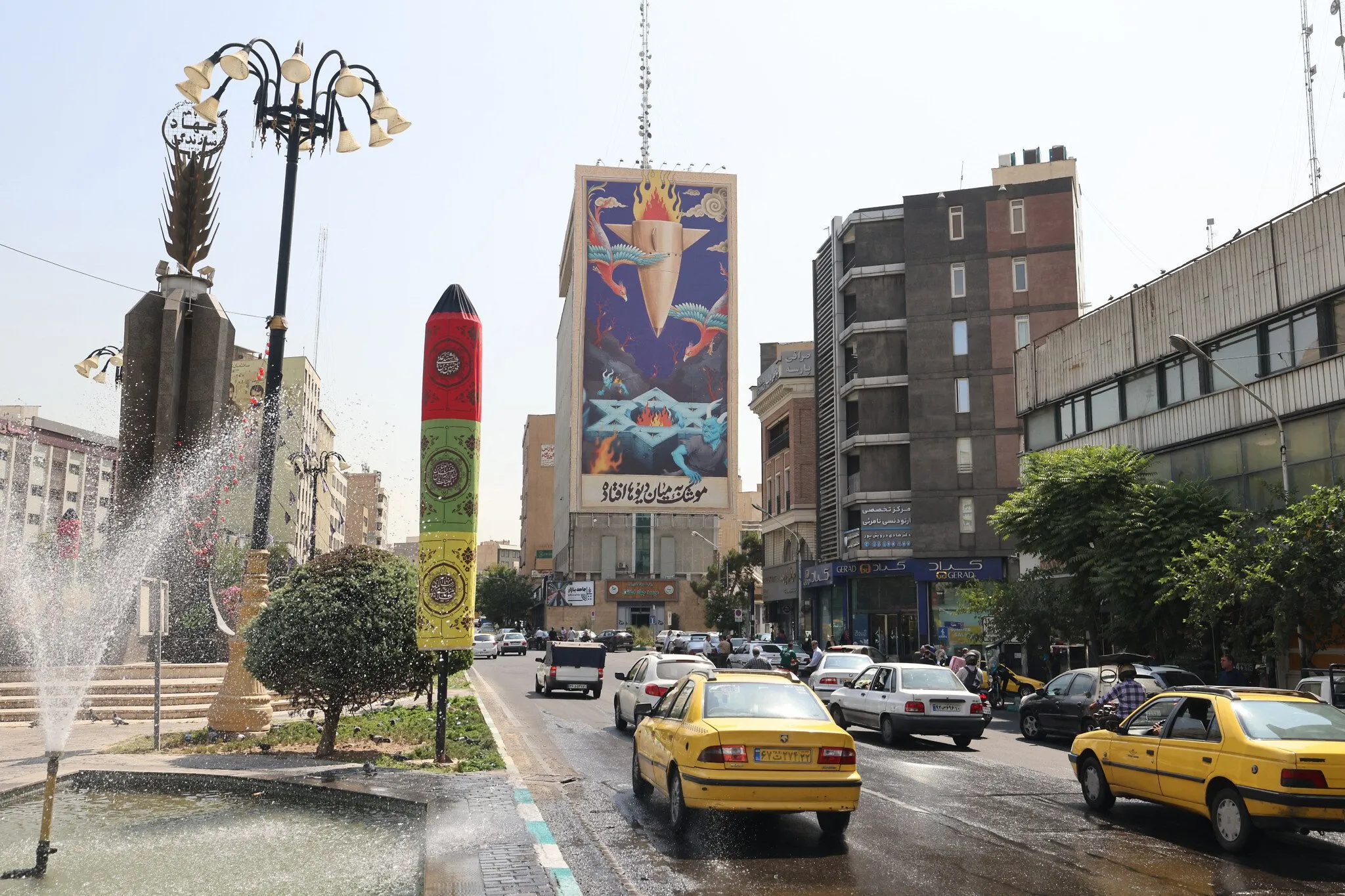El tráfico fluye en Teherán junto a una enorme valla publicitaria con una pintura de un misil cayendo sobre Israel con el lema en farsi, “El misil ha caído entre los demonios”, el 16 de julio de 2025 (ATTA KENARE / AFP)