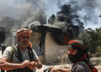 Combatientes beduinos frente a una tienda incendiada en la aldea de Mazraa, en las afueras de la ciudad de Sweida, durante los enfrentamientos entre los clanes beduinos y las milicias drusas, en el sur de Siria, el viernes 18 de julio de 2025. (AP Foto/Ghaith Alsayed)
