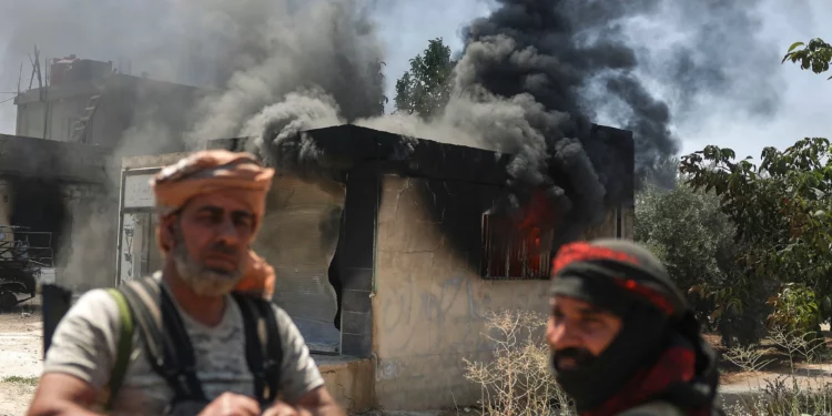 Combatientes beduinos frente a una tienda incendiada en la aldea de Mazraa, en las afueras de la ciudad de Sweida, durante los enfrentamientos entre los clanes beduinos y las milicias drusas, en el sur de Siria, el viernes 18 de julio de 2025. (AP Foto/Ghaith Alsayed)
